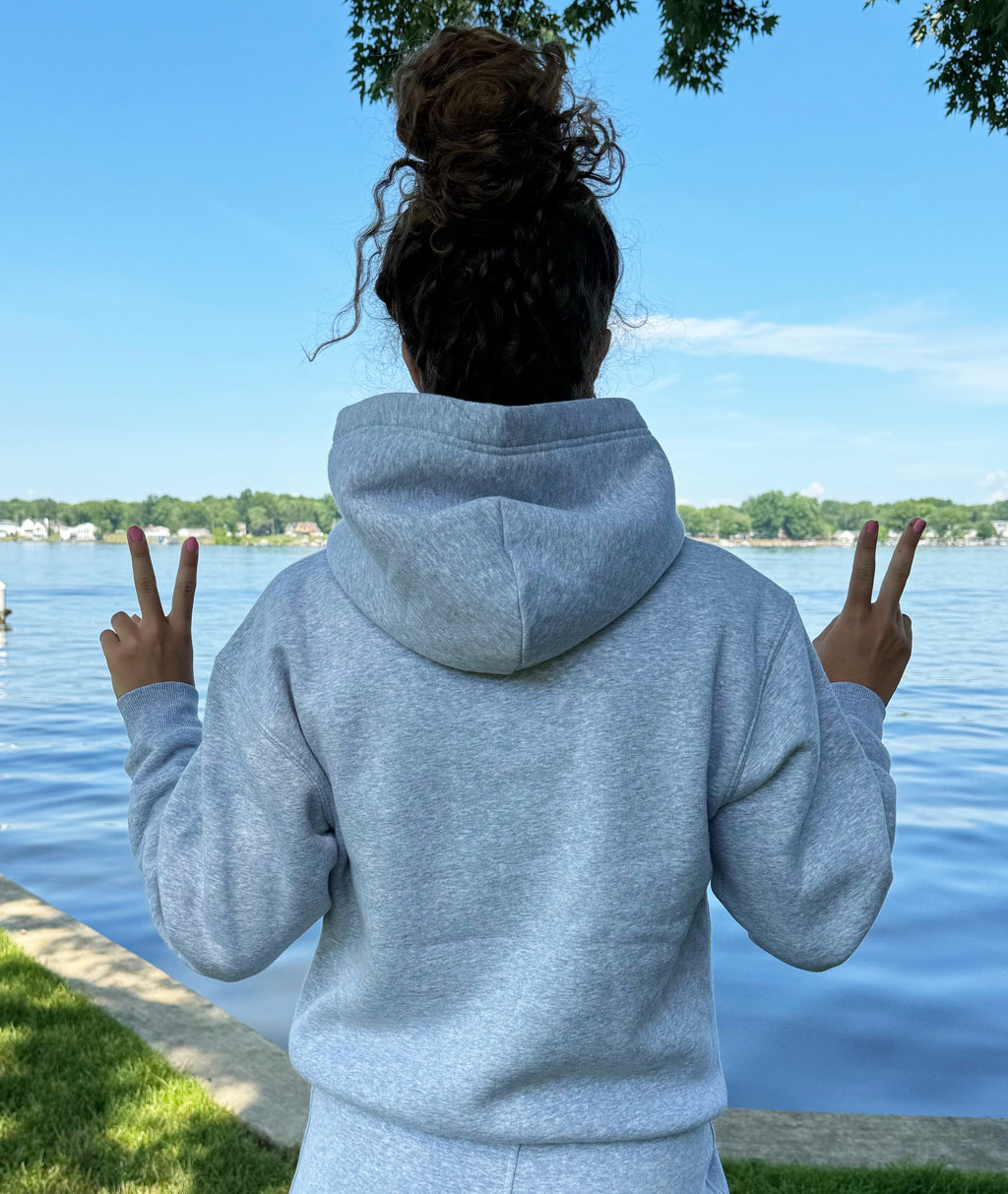 Person wearing a gray hoodie with 'Alpha Omicron Pi' text in red, standing by a body of water.