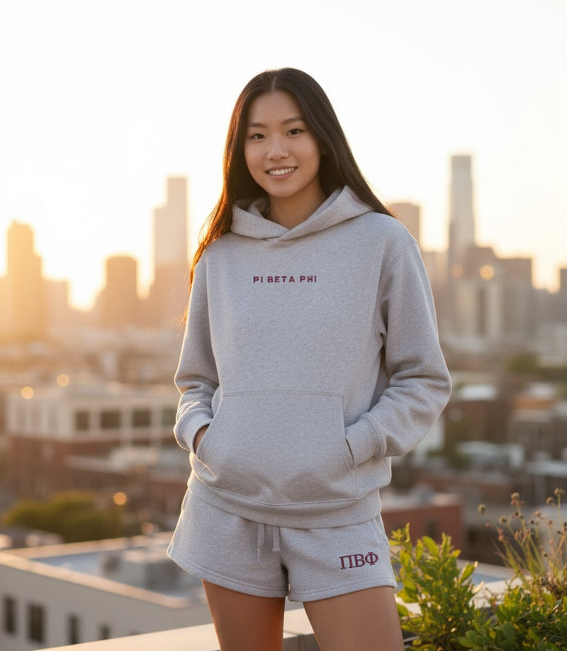 Person wearing a gray hoodie and shorts with 'Pi Beta Phi' on a rooftop with city skyline in the background
